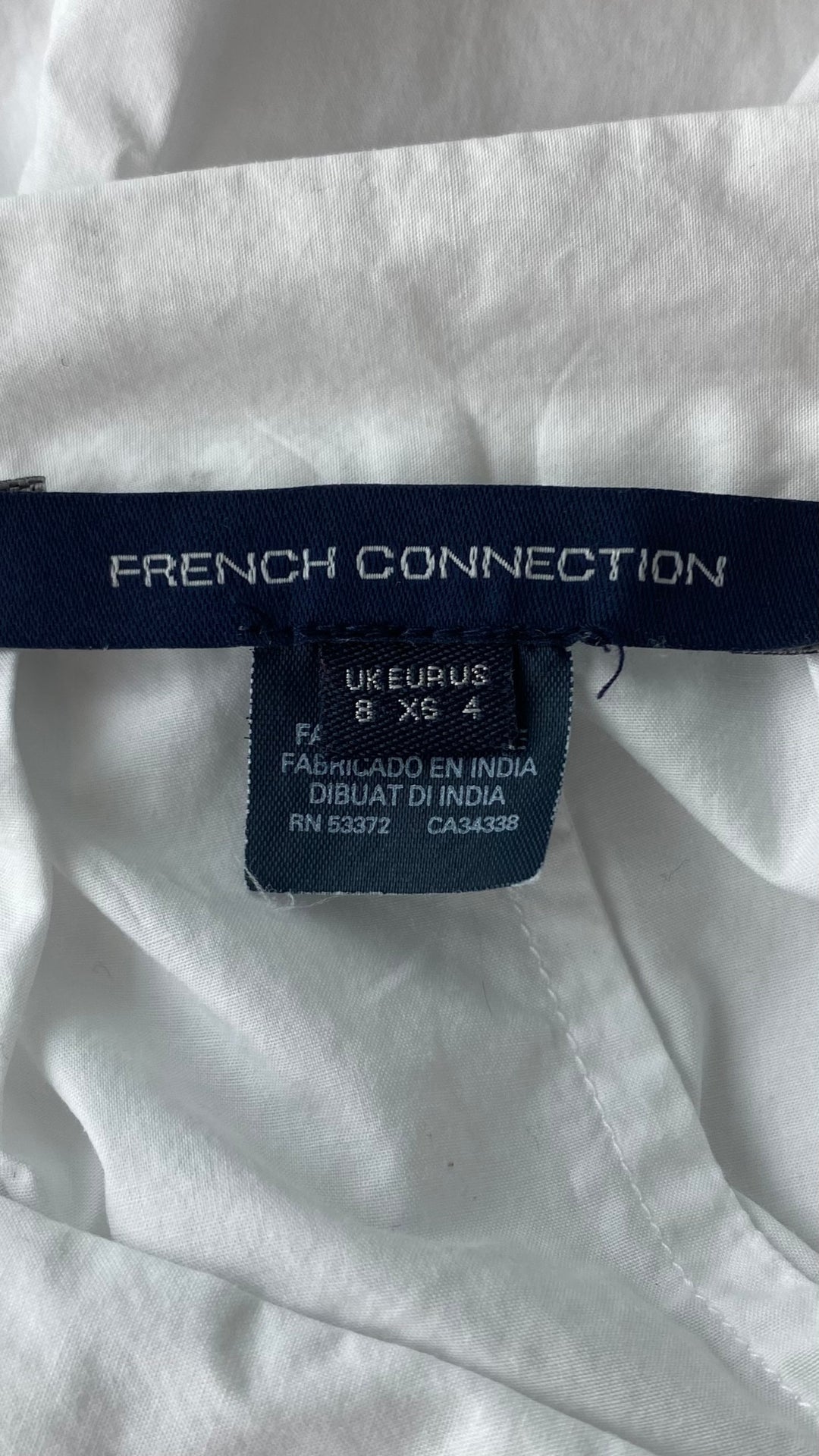 Pantalon très ample blanc style jupe avec broderie anglaise au bas des jambes. Marque French Connection, taille extra small, équivalent à 4. Vue de l'étiquette de marque et taille.