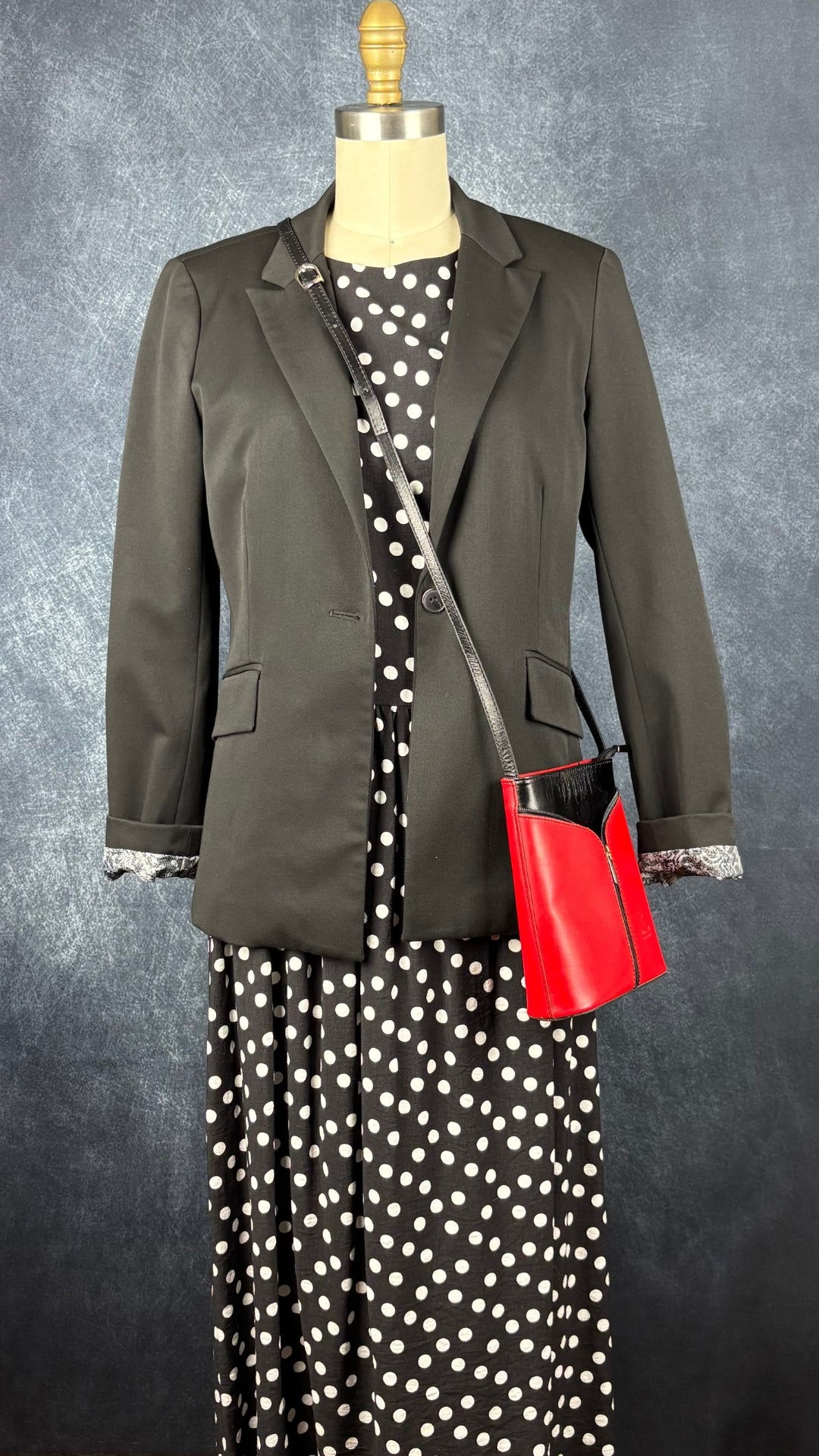 Sac à main en cuir noir et rouge à bandoulière Vera Pelle avec base ovale Vera Pelle. Vue de l'agencement avec la robe à pois Mimz et le blazer noir lavable Tristan.