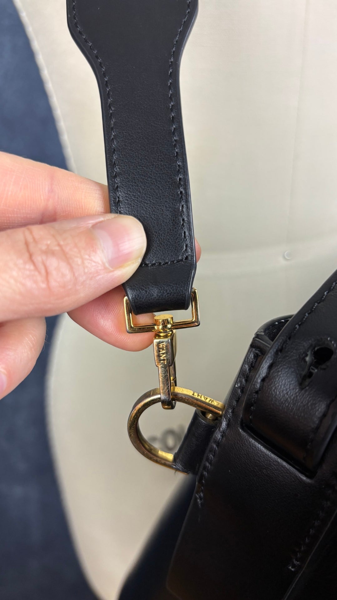 Sac sceau noir à poignée et bandoulière en cuir Want Les Essentiels. Vue de près d'une pièce de quincaillerie qui permet de retirer la courroie.