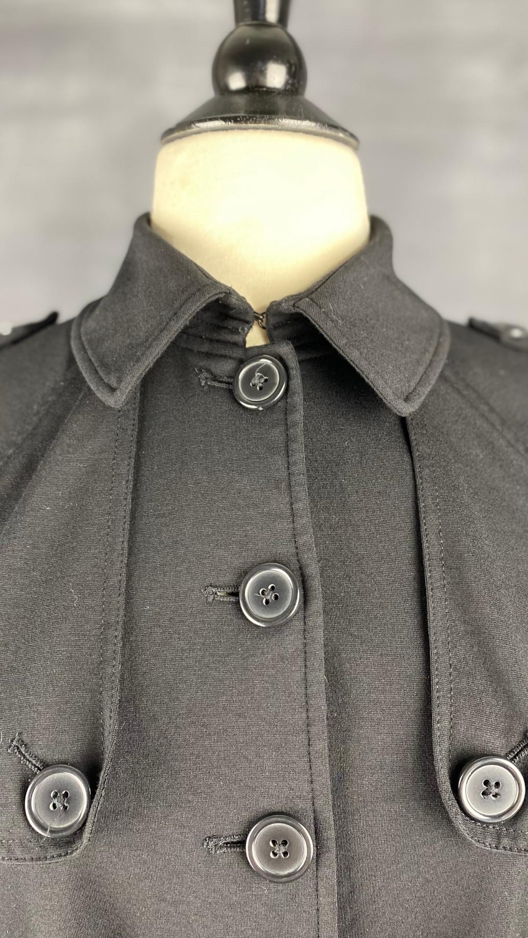 Veste courte noire façon trench. Extensible et polyvalente, les manches se roulent et sont maintenues en place à l'aide d'une sangle. Ceinturée à la taille. Vue rapprochée du col.