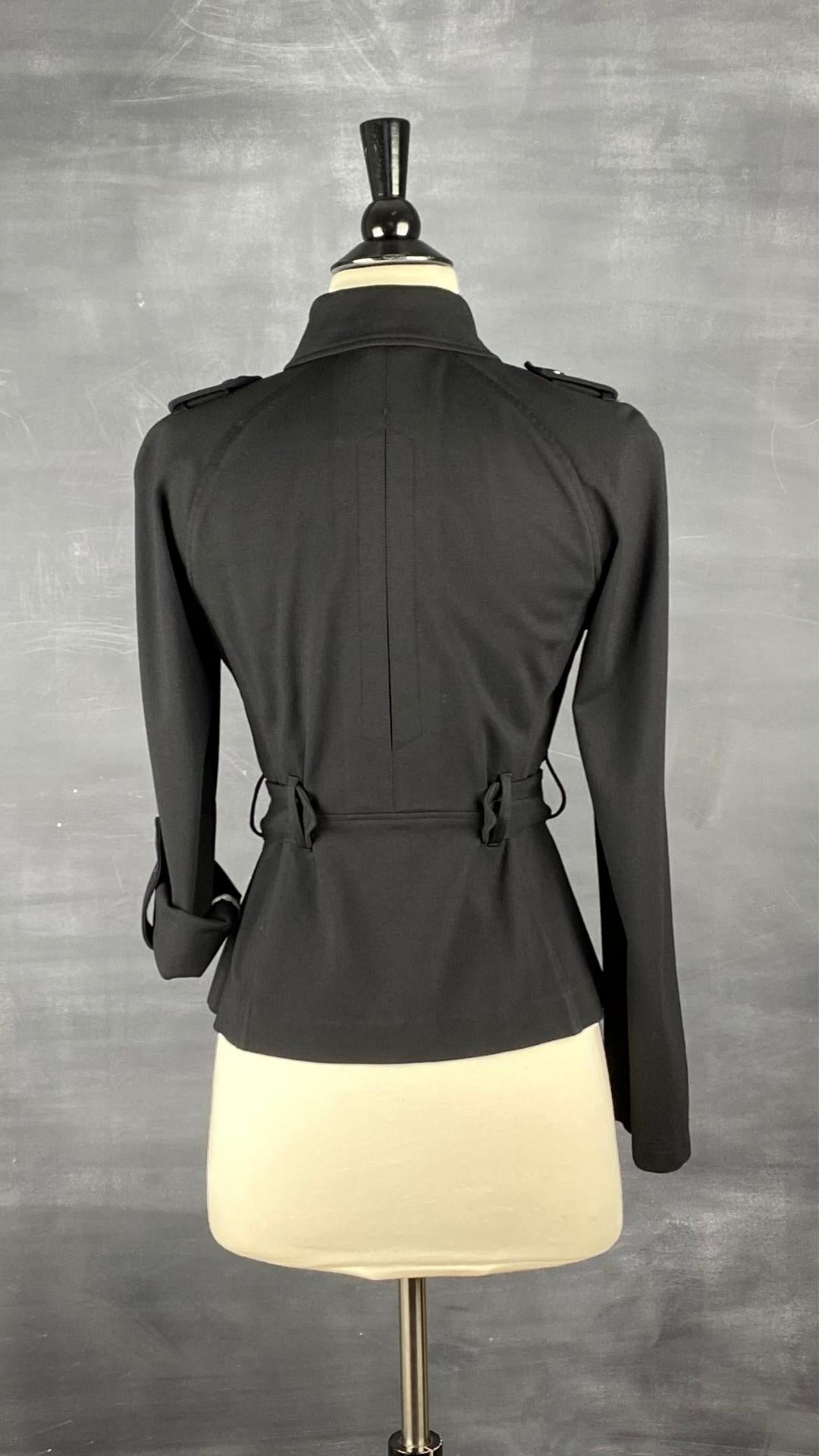 Veste courte noire façon trench. Extensible et polyvalente, les manches se roulent et sont maintenues en place à l'aide d'une sangle. Ceinturée à la taille. Vue de dos.