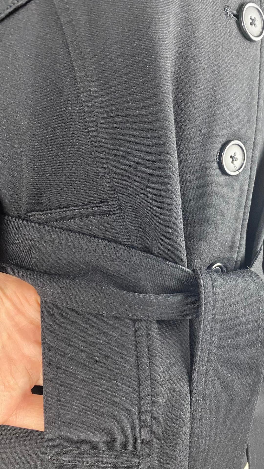Veste courte noire façon trench. Extensible et polyvalente, les manches se roulent et sont maintenues en place à l'aide d'une sangle. Ceinturée à la taille. Vue de la poche.