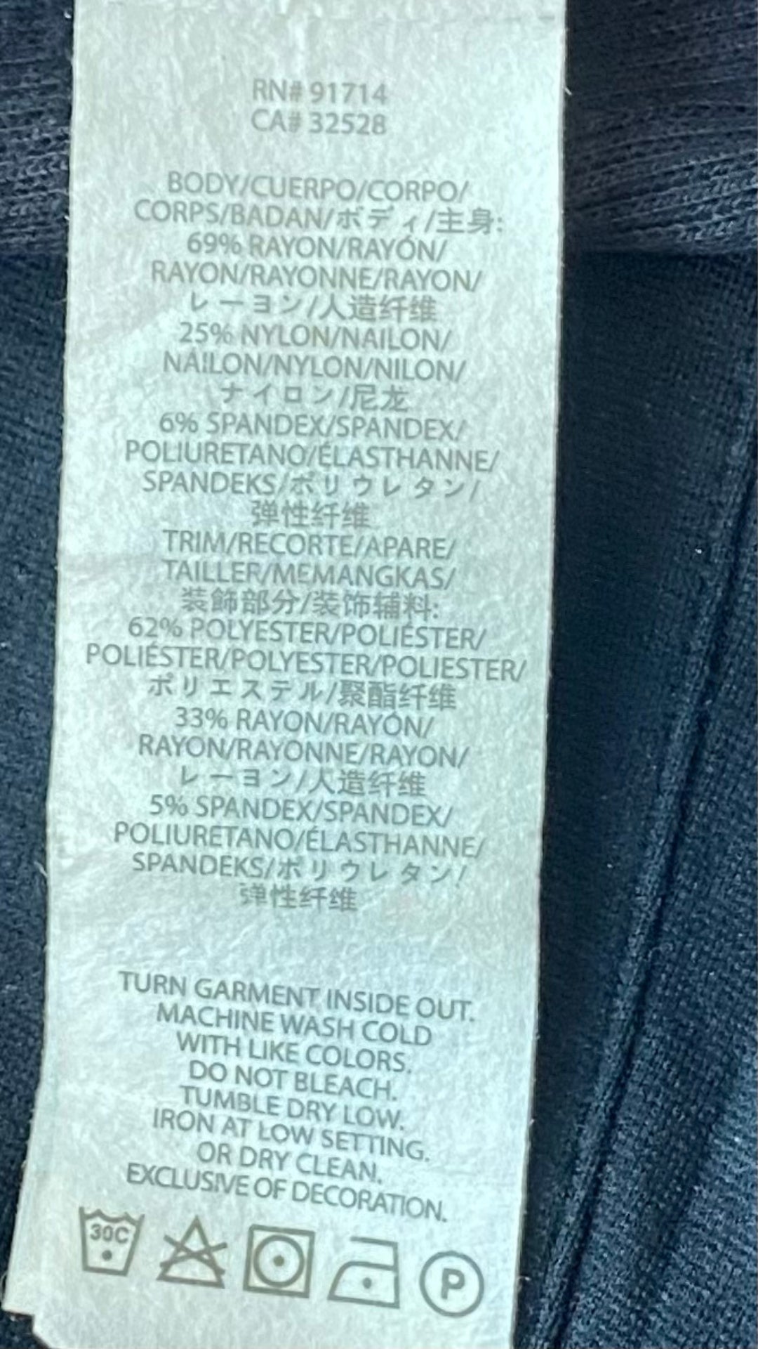 Veste noire à grand col zippé, légèrement décentré. Vue de l'étiquette de composition et entretien.