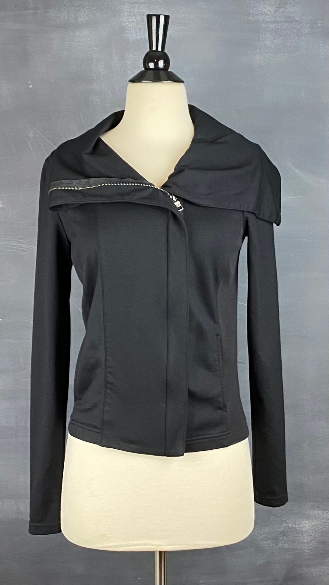 Veste noire à grand col zippé, légèrement décentré. Vue de face.