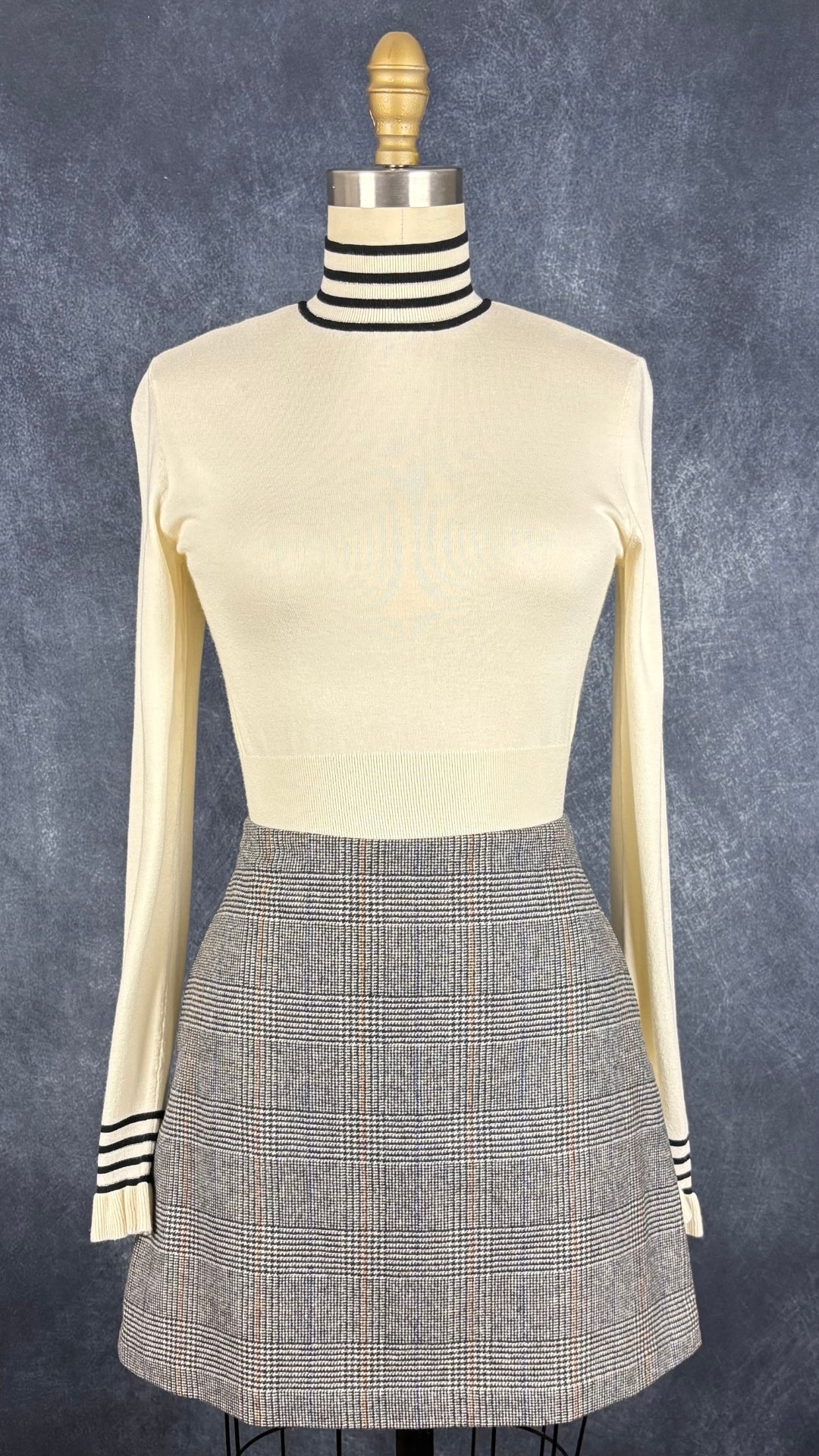 Chandail crème à col montant à ourlets à rayures noires et argentées Tristan, taille small. Vue de l'agencement avec la jupe à carreaux prince-de-galles Wilfred.