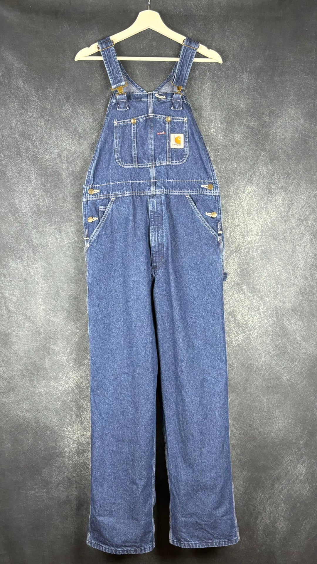 Salopette en jeans foncé Carhartt, taille 32. Vue de face, pleine longueur sur un cintre.