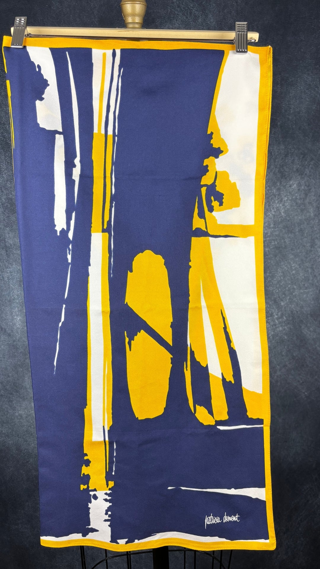 Foulard floral marine et jaune Patricia Dumont, carré. Vue du foulard plié en deux sur un cintre, côté avec motifs abstraits et marque.