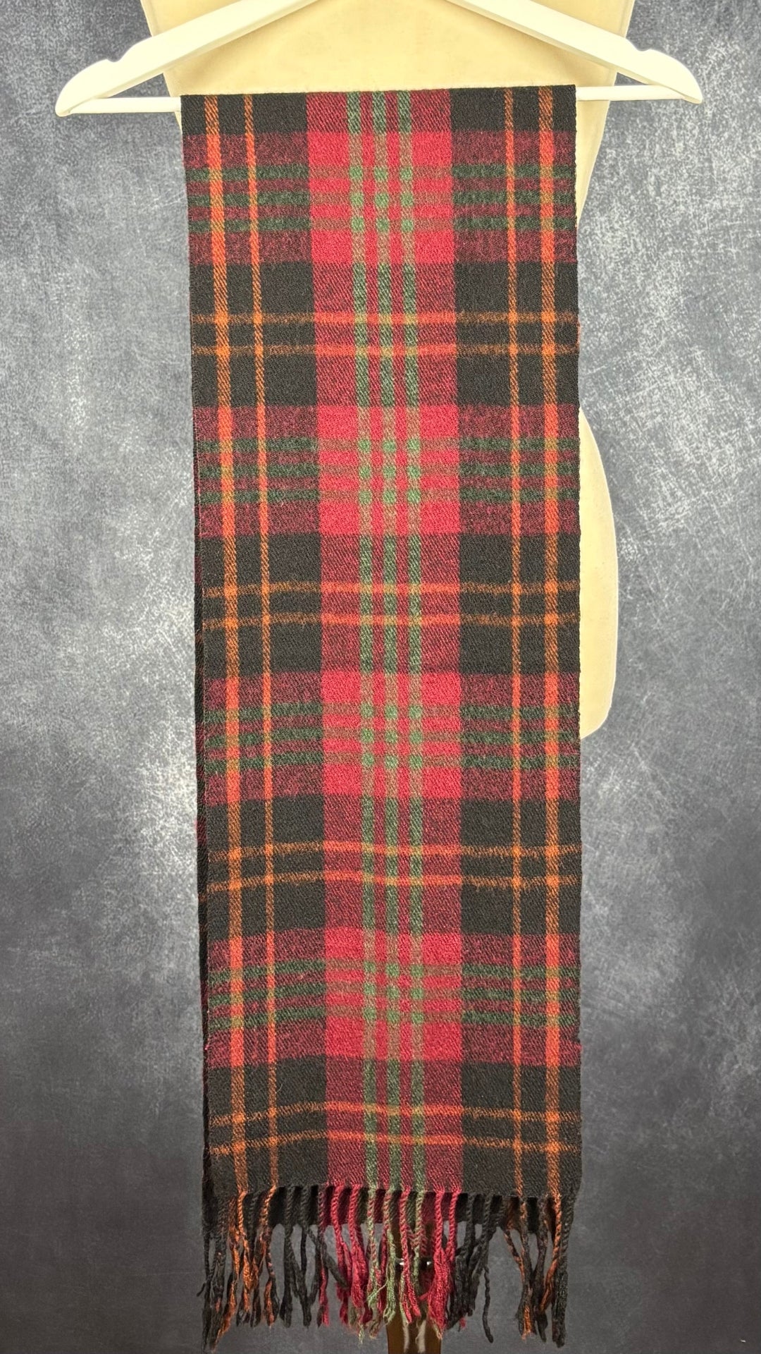 Foulard en lainage à carreaux Woolrich rectangulaire. Vue du foulard, plié en deux sur un cintre.