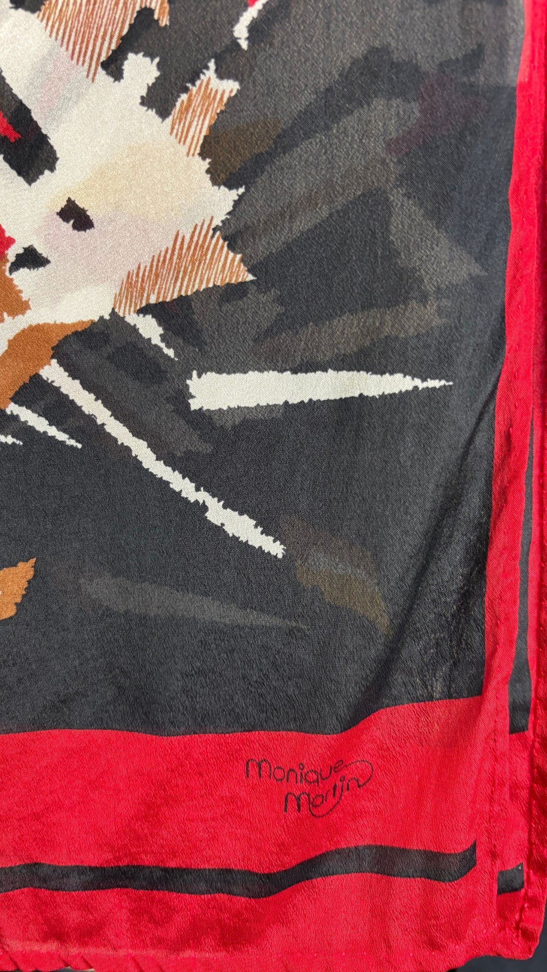 Foulard noir, blanc et rouge Monique Martin, rectangulaire long. Vue de la marque inscrite sur le coin du foulard.