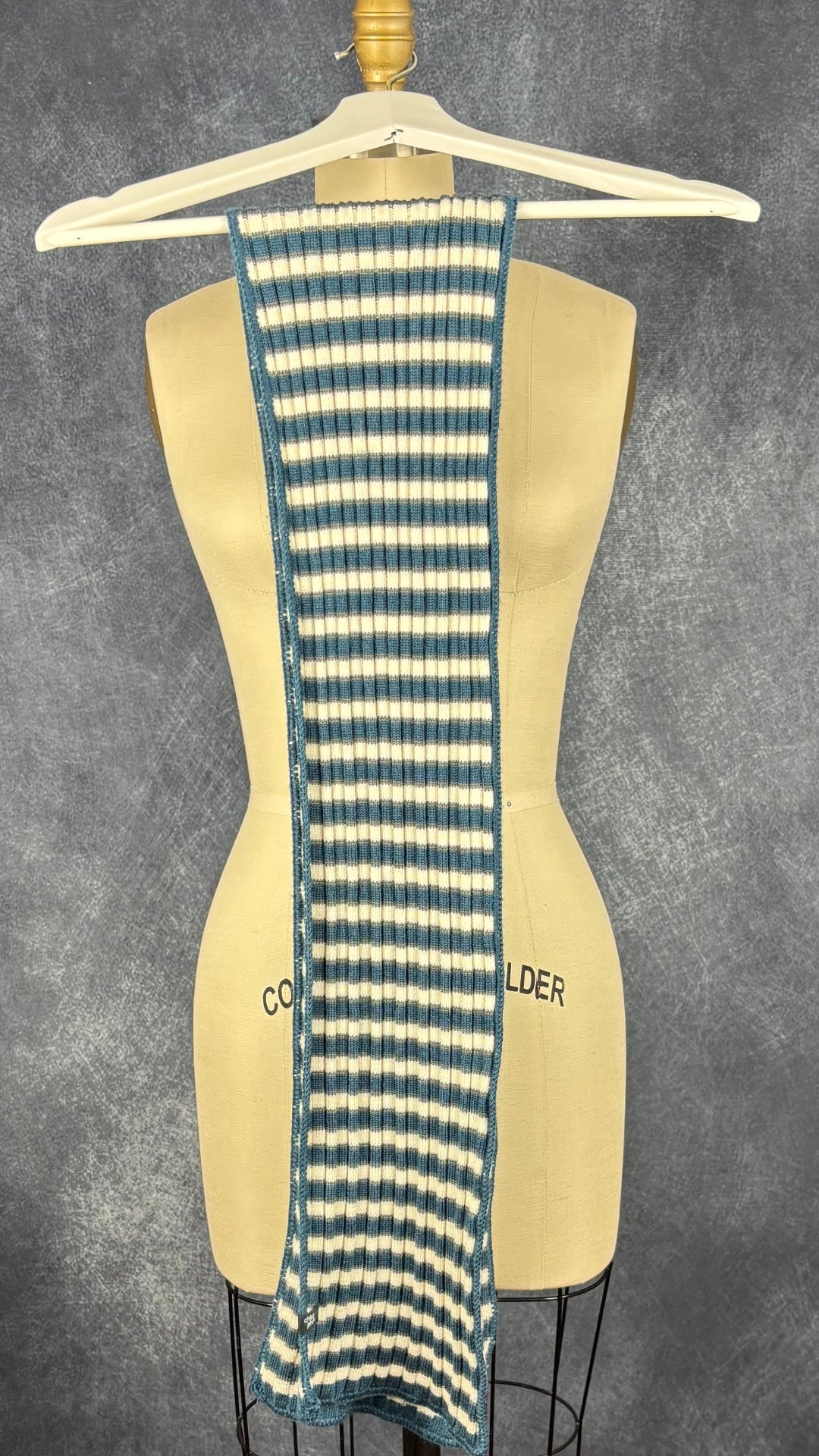 Foulard en tricot à rayures Chlorophylle, taille rectangulaire étroit. Vue du foulard plié en deux sur un cintre.