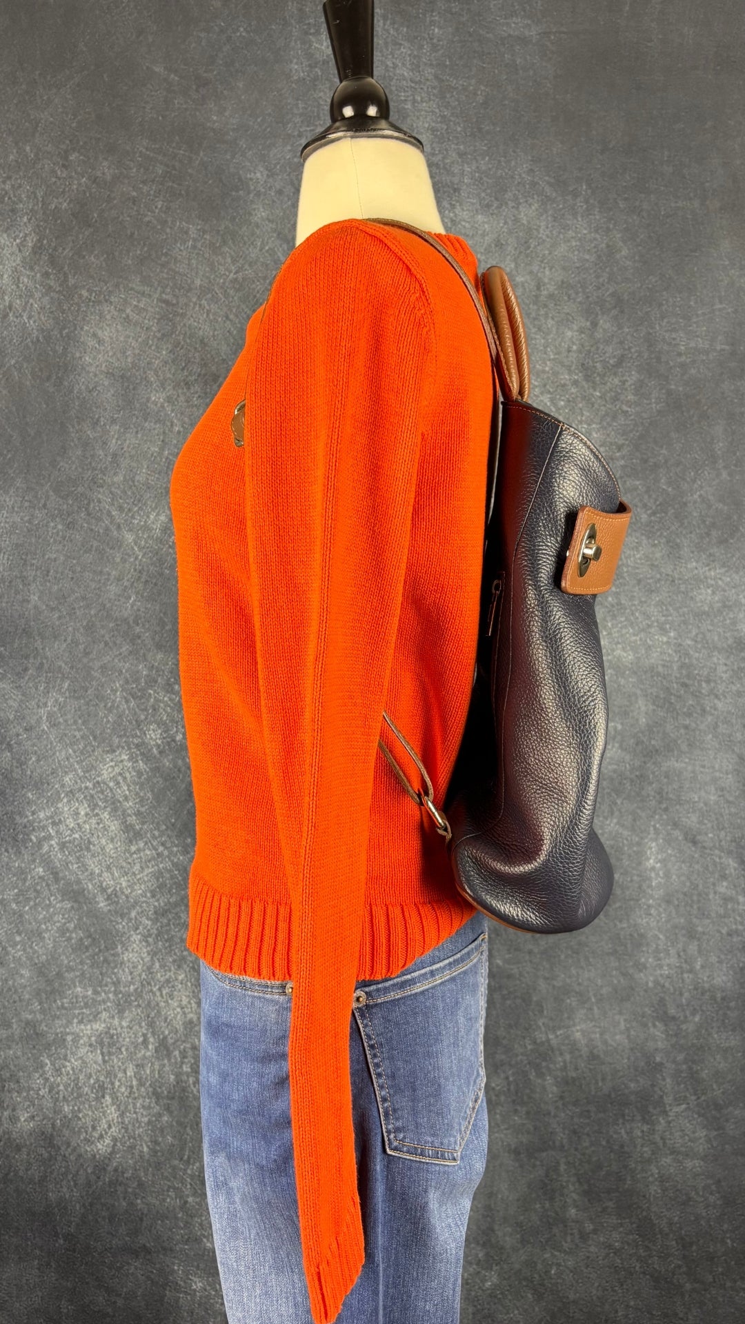 Jeans évasé coupe style bootcut, délavage bleu moyen, Yoga Jeans, taille 27. Vue de côté de l'agencement avec le chandail en tricot de coton orange et le sac à dos Vera Pelle.