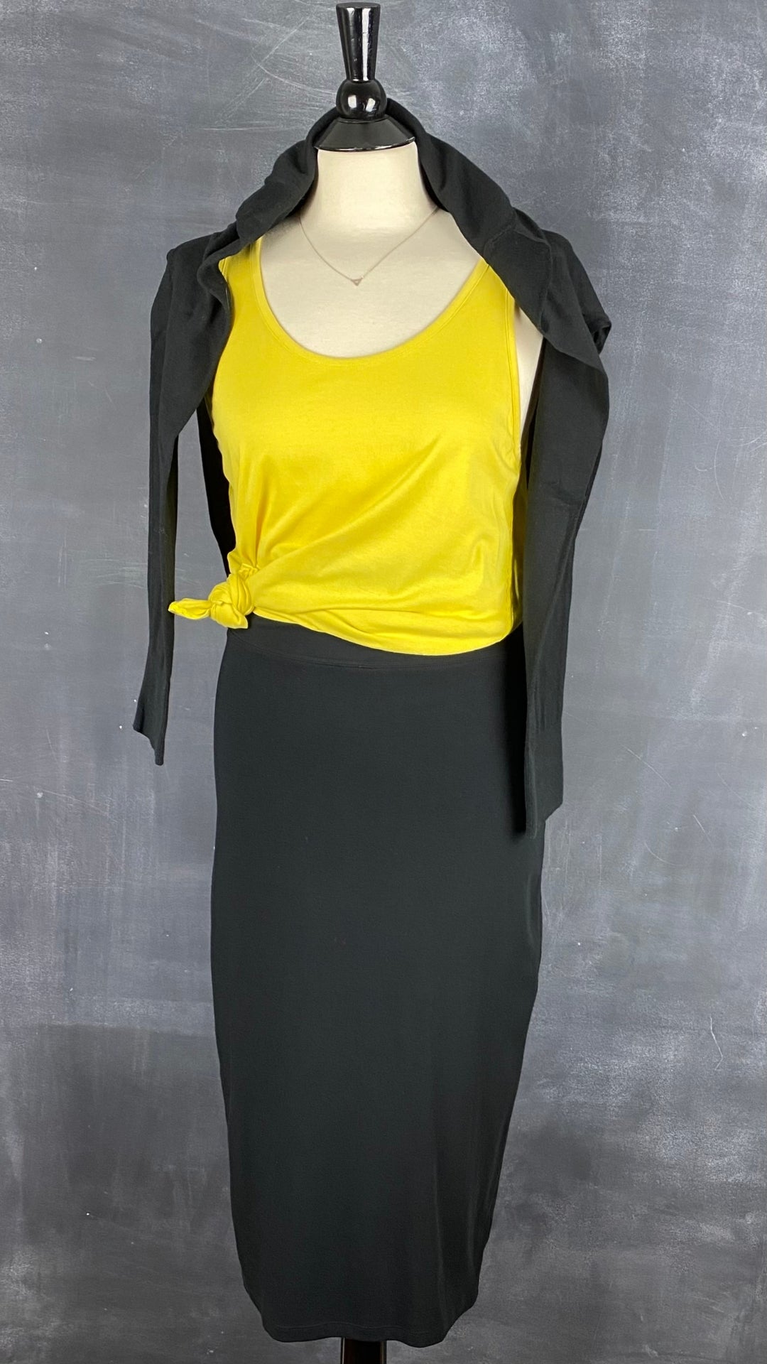 Jupe midi noire extensible Babaton, taille medium (small). Vue de l'agencement avec une camisole jaune et un cardigan noir.