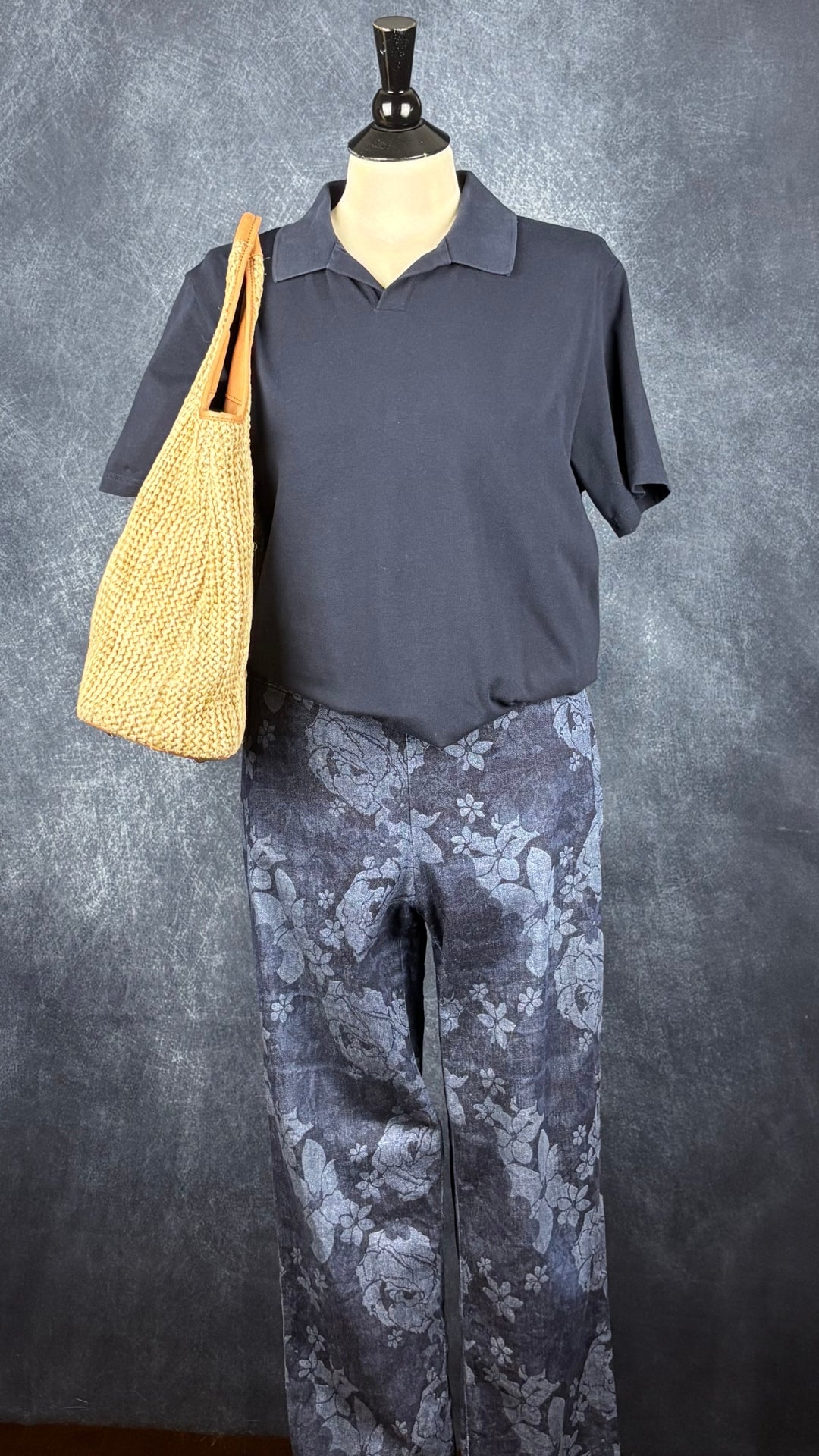 Pantalon style denim à motif floral Lisette L Signature, taille estimée à large. Vue de l'agencement avec le polo marine Filippa K et un sac en paille.