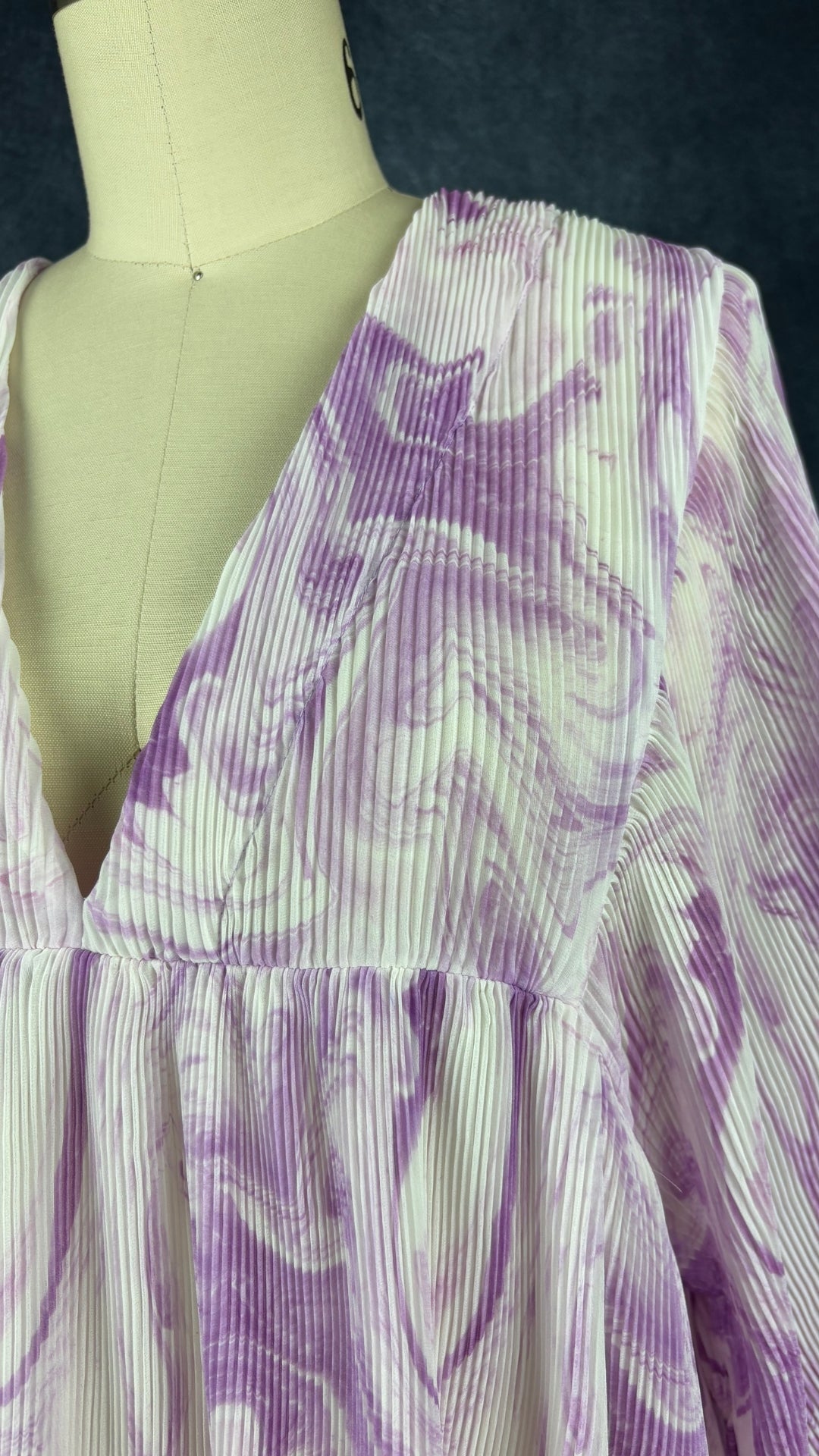 Robe à motifs de tourbillons lilas et mauve, finement plissée Ganni, taille s/m. Vue de près du décolleté.