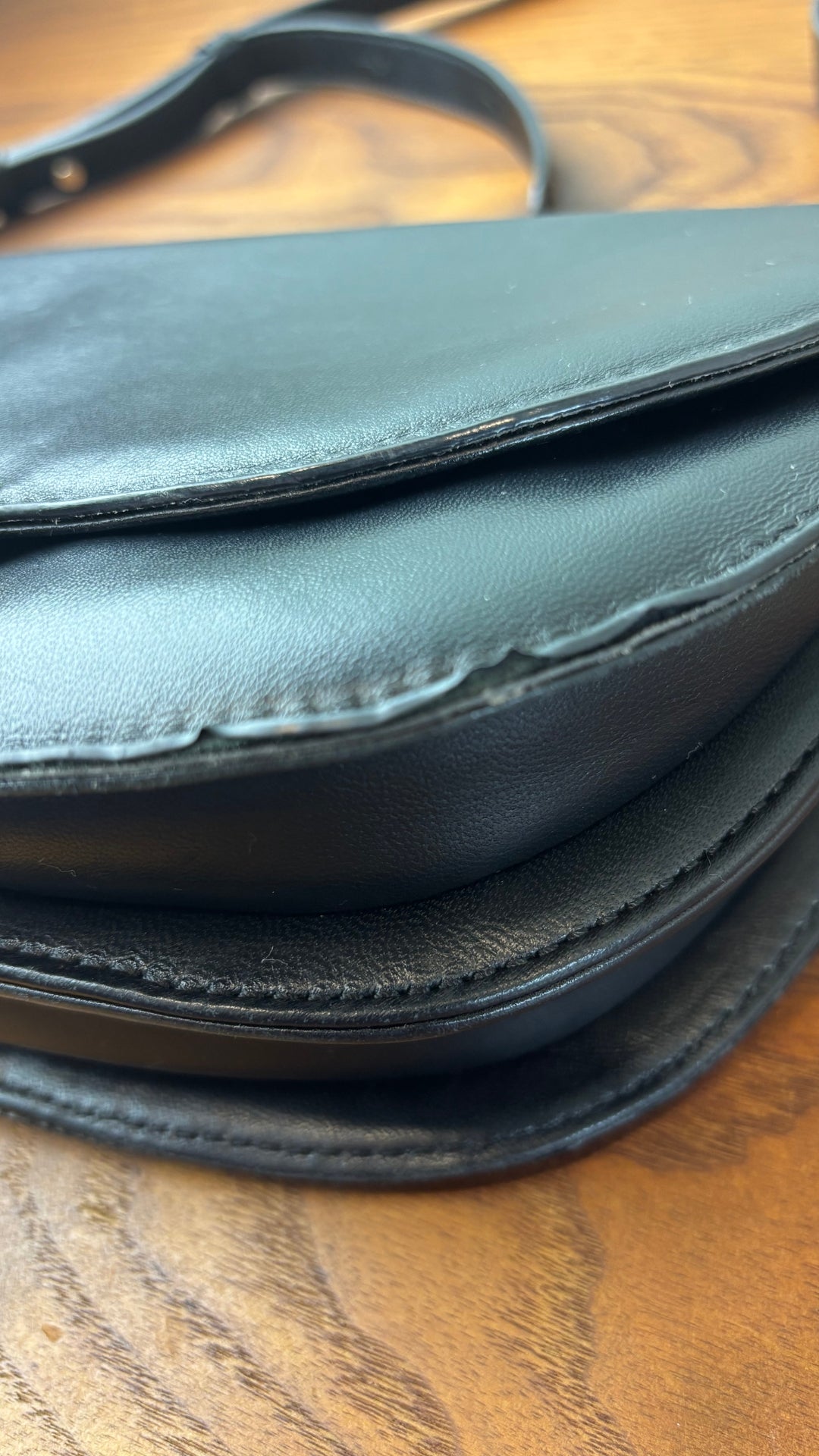 Sac en cuir lisse en demi-lune avec courroie type bandoulière, Flattered. Vue de près du coin gauche du sac.