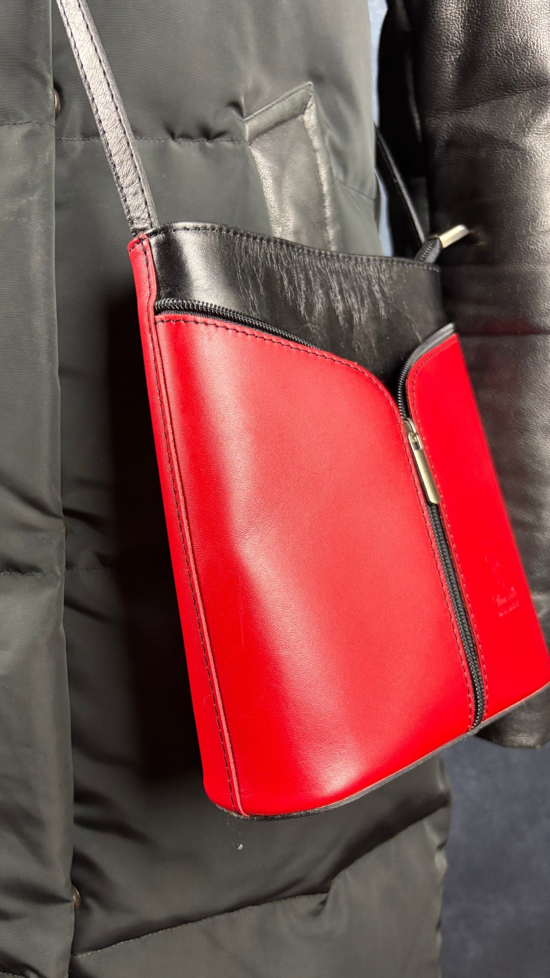 Sac à main en cuir noir et rouge à bandoulière Vera Pelle avec base ovale Vera Pelle. Vue de demi côté, sur le manteau Rudsak.
