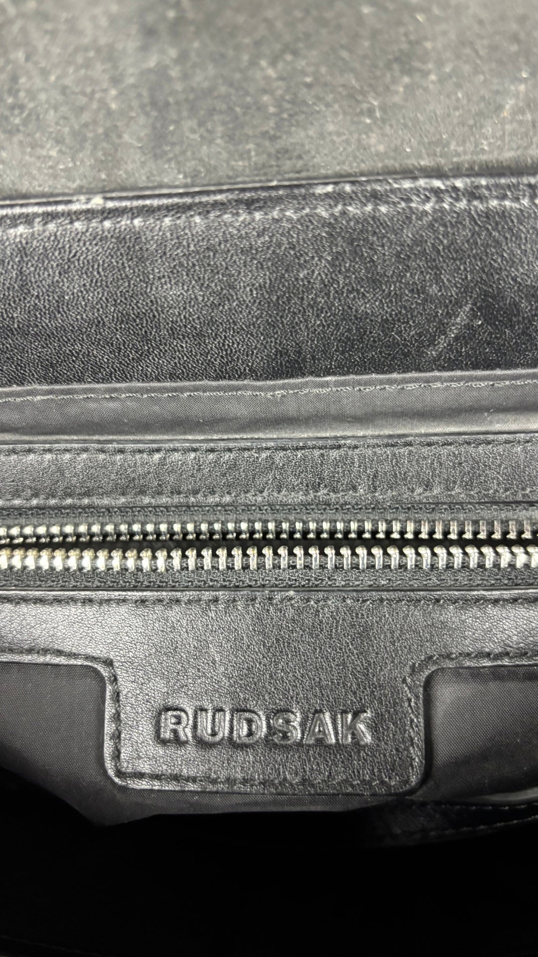 Sac à main en cuir noir Rudsak de taille moyenne avec coins de la base arrondis. Vue de l'étiquette de la marque à l'intérieur.