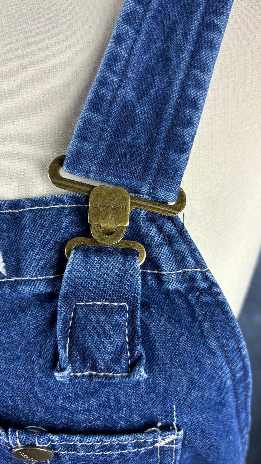 Salopette en jeans foncé Carhartt, taille 32. Vue de près de l'attache de la bretelle.