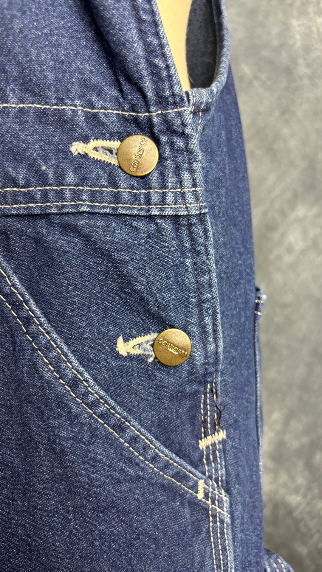 Salopette en jeans foncé Carhartt, taille 32. Vue des boutons sur les côtés.