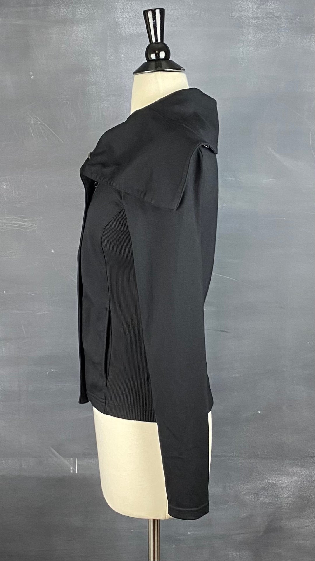 Veste noire à grand col zippé, légèrement décentré. Vue de côté.